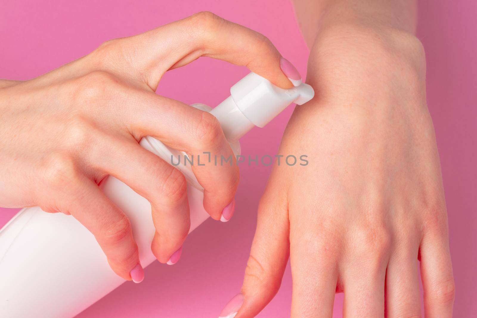 Female hand holding skincare product bottle on pink background