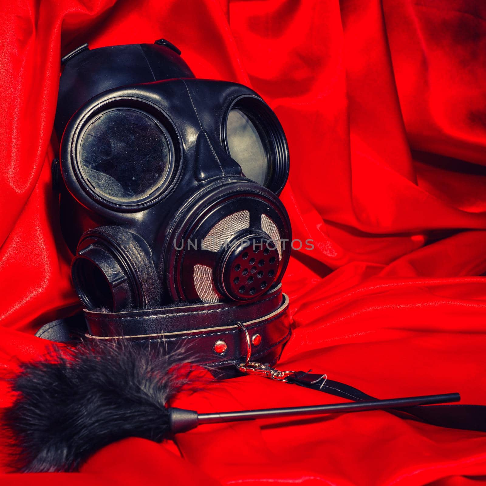 Close up bdsm outfit. Bondage, kinky adult sex games, kink and BDSM lifestyle concept with gas mask, feather stick on red silk with copy space. Toned