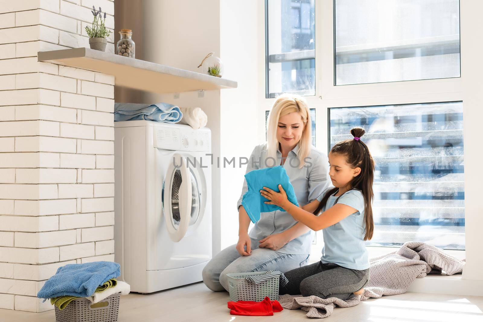 Happy housewife and her daughter with linen near washing machine