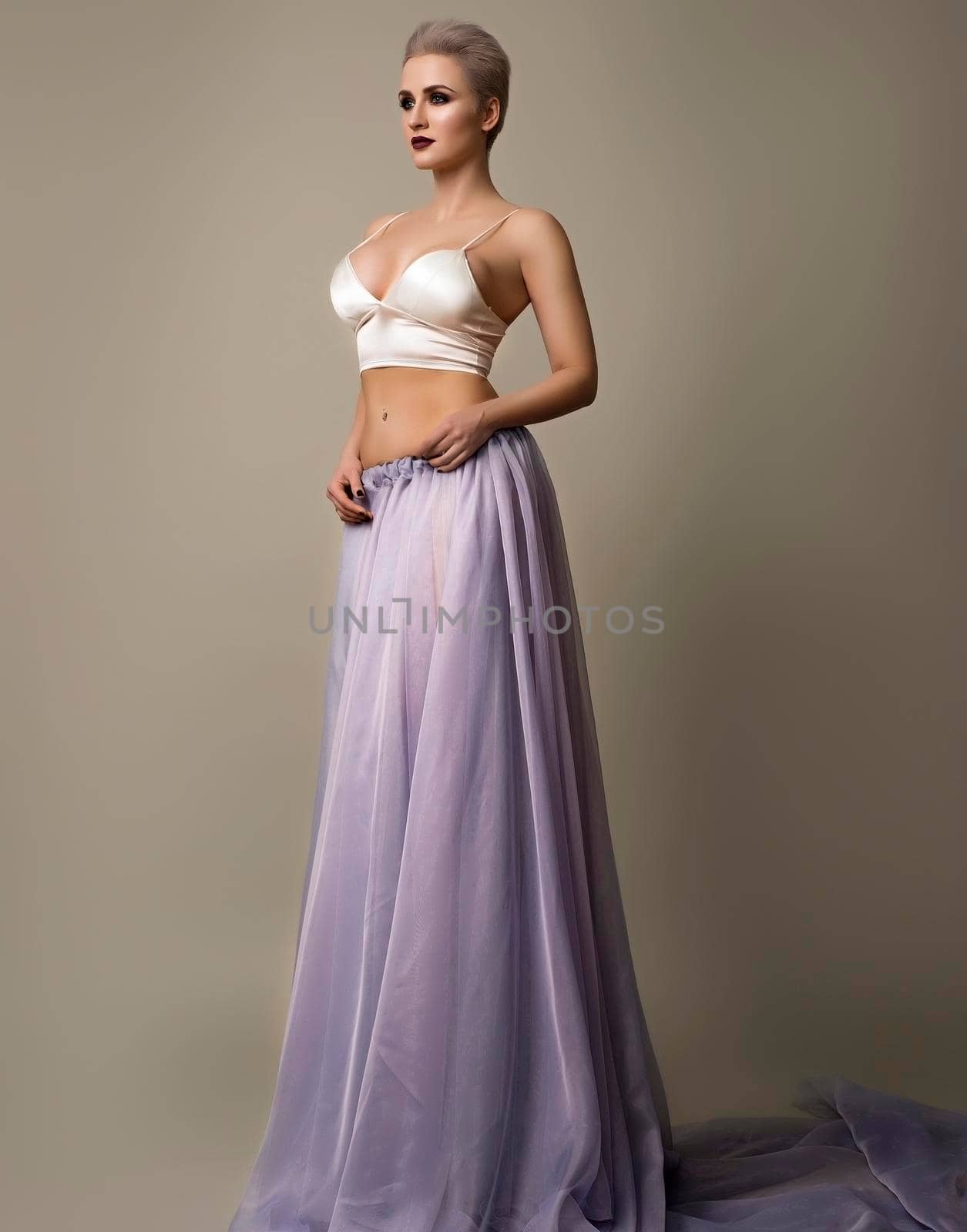 Young stylish woman with short haircut in white bra and transparent skirt posing on gray background by zartarn