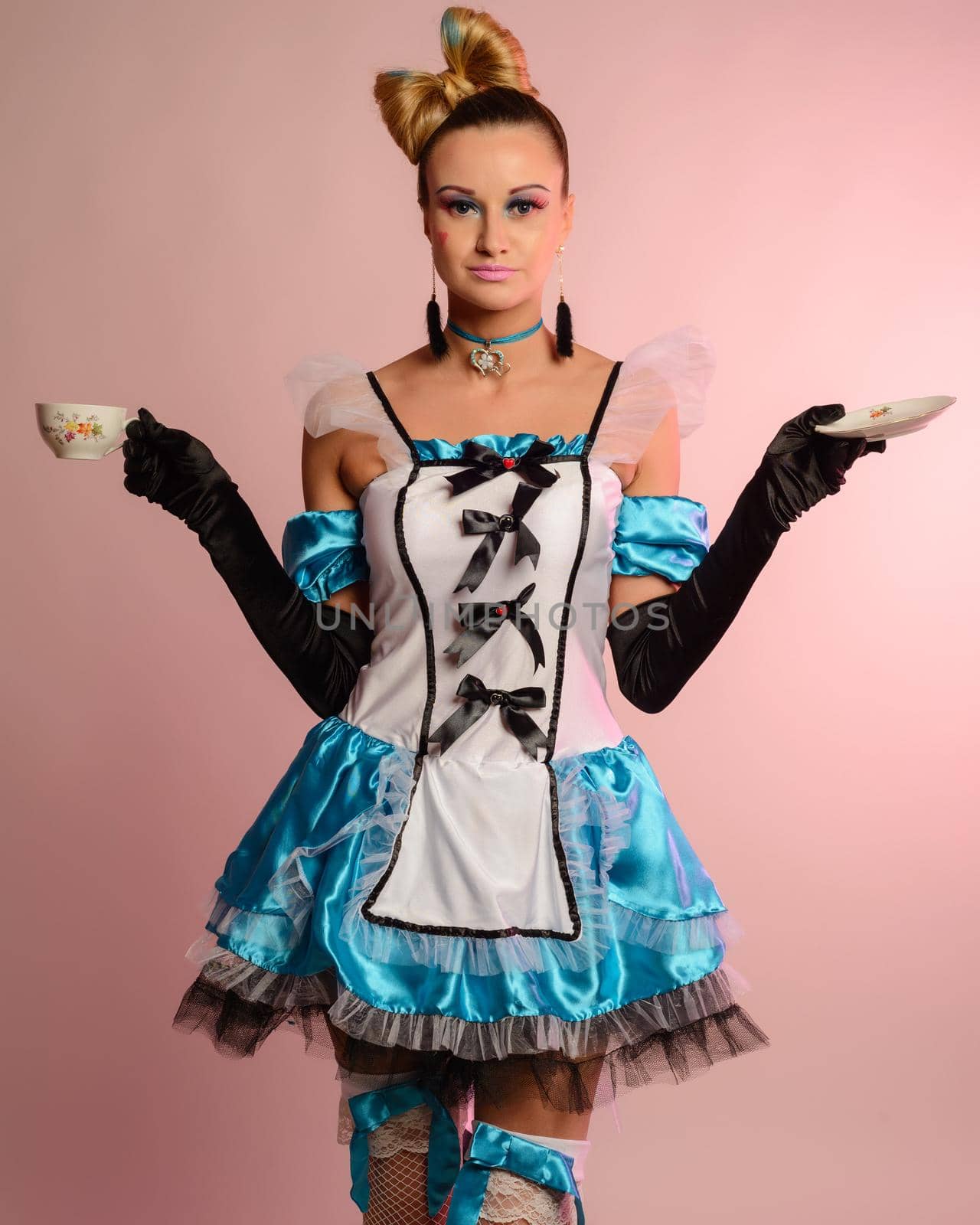 Young slim woman in erotic dress alice in wonderland holds a cup and saucer on a pink background.