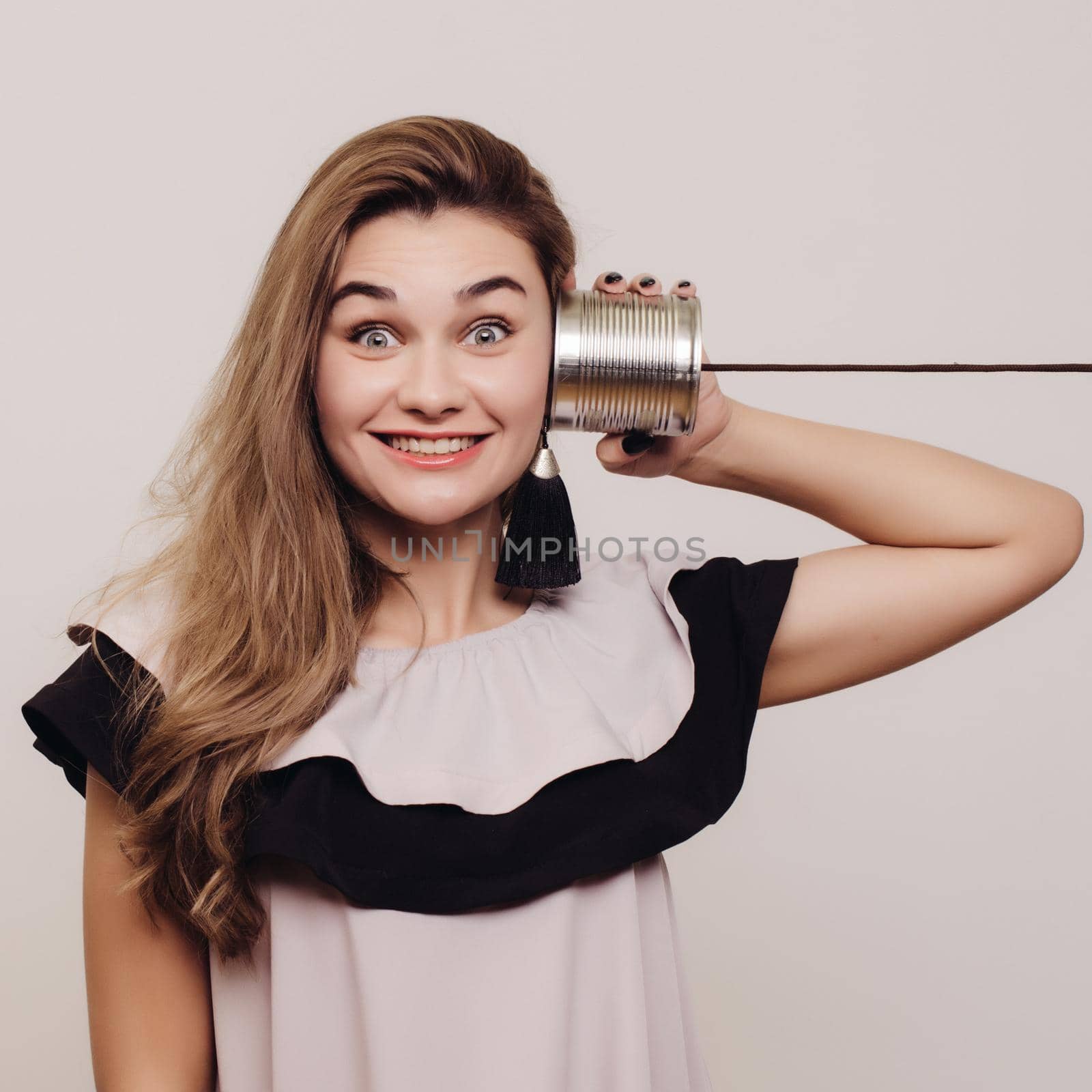 portrait of young woman hearing through a tin can over grey.