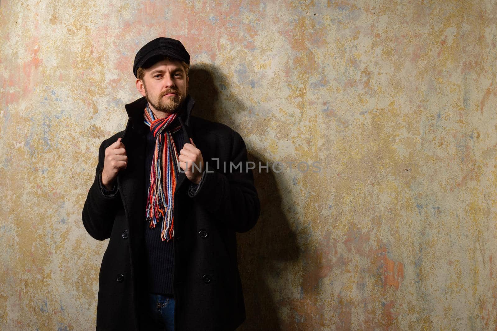 image of a caucasian man with grungy blond hair dressed warmly in a stylish black trench coat and a funky hat and scarf for the cold winter