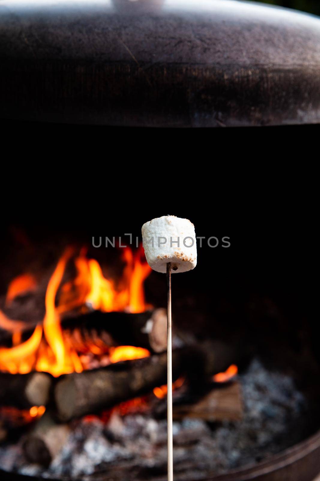 Person roasting over fire flames a marshmallows over campfire at night on a summer day, for smores or snack closeup