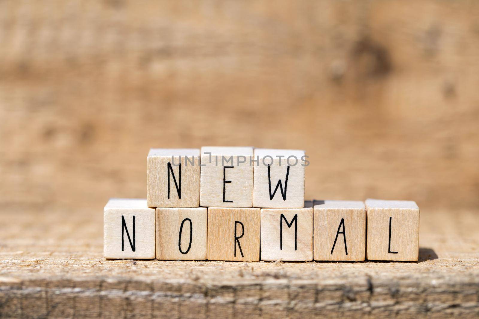 NEW NORMAL text on wooden cube. New normal life after covid-19 pandemic with social distancing and good hygiene on wooden background closeup