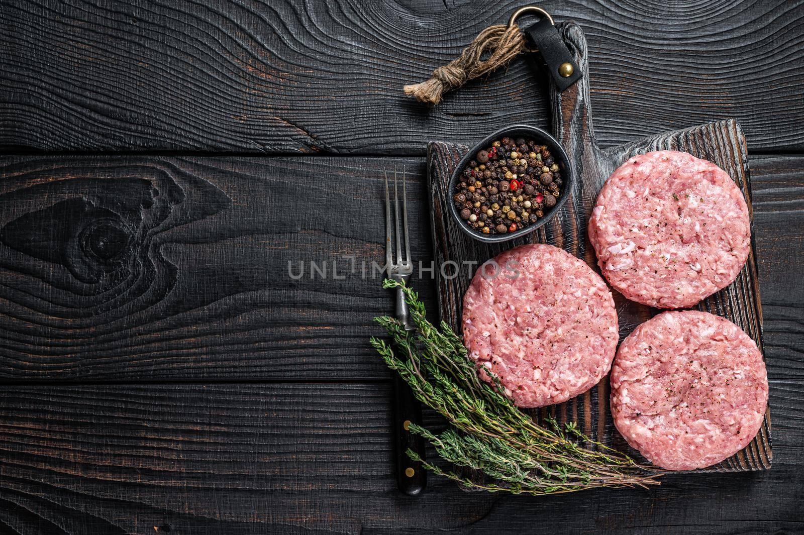 Raw chicken turkey patty, ground meat cutlets on a chopping Board. Black wooden background. Top view. Copy space by Composter