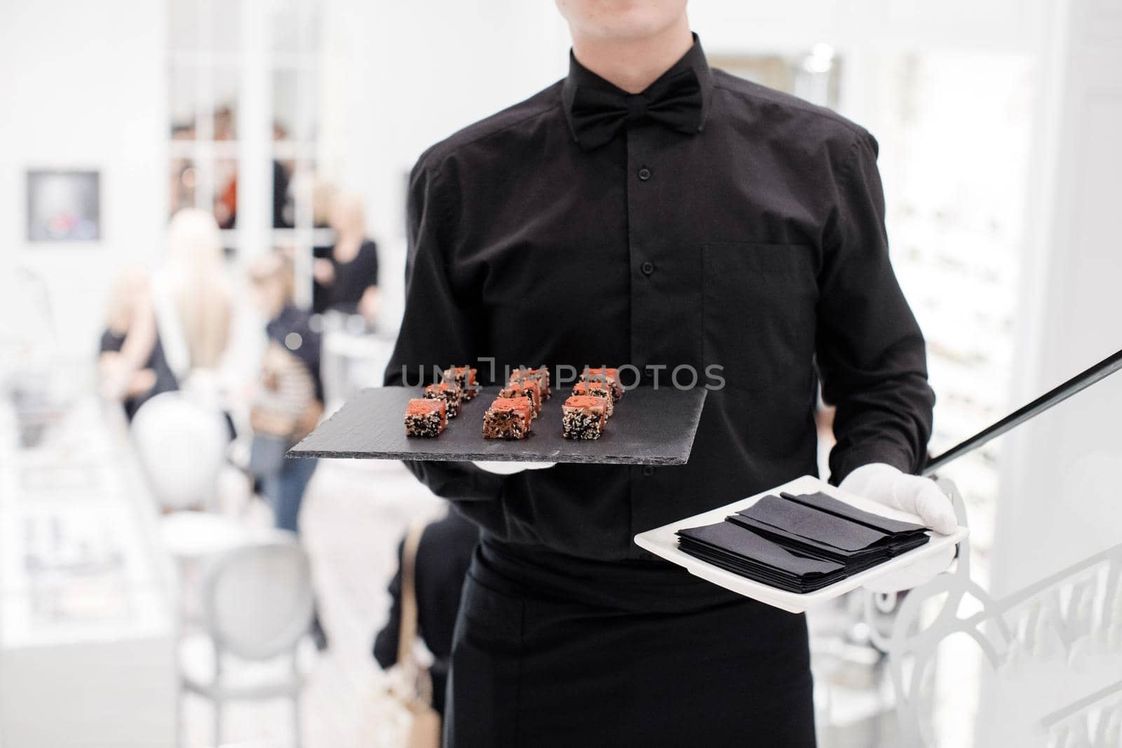 Crop man in black uniform and white gloves serving rolls on stone plate in restaurant