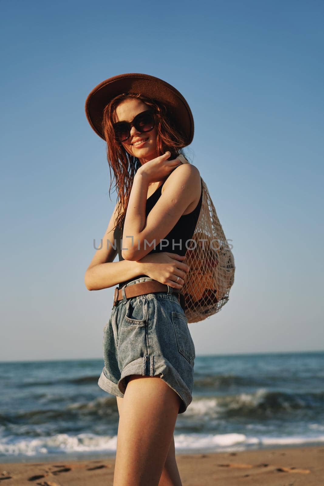 cheerful woman in a hat with sunglasses walking with a bag by Vichizh