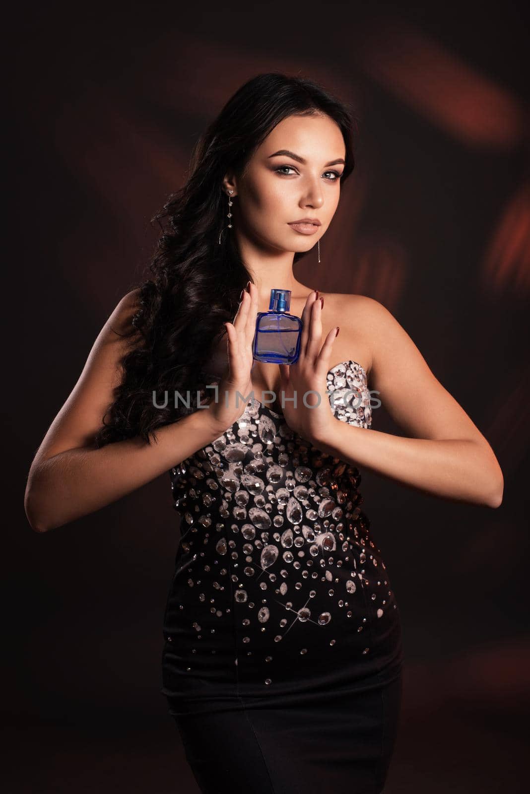 Beautiful young woman in a shiny dress with a bottle of perfume.