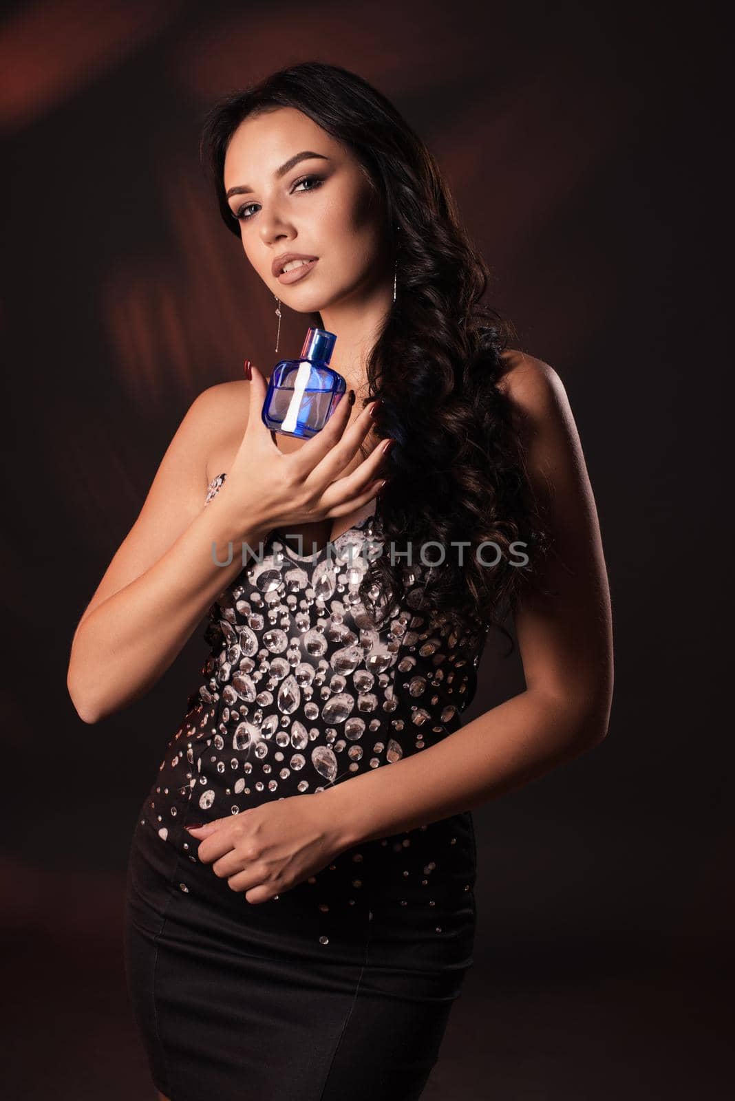 Portrait of a beautiful girl in a black crystals dress with spirits in hands.