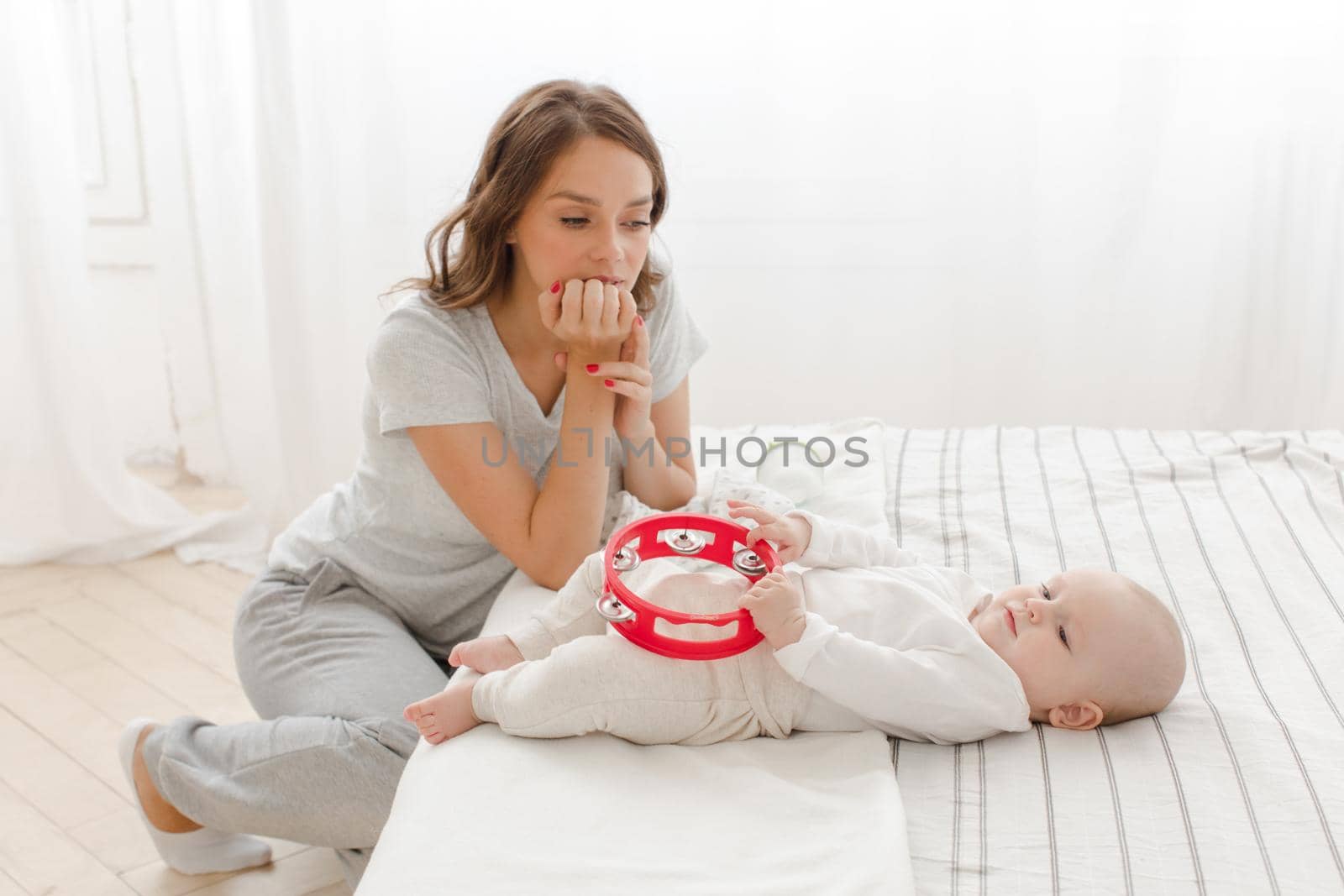 Young woman looking at charming baby on bed with love and tender in light.