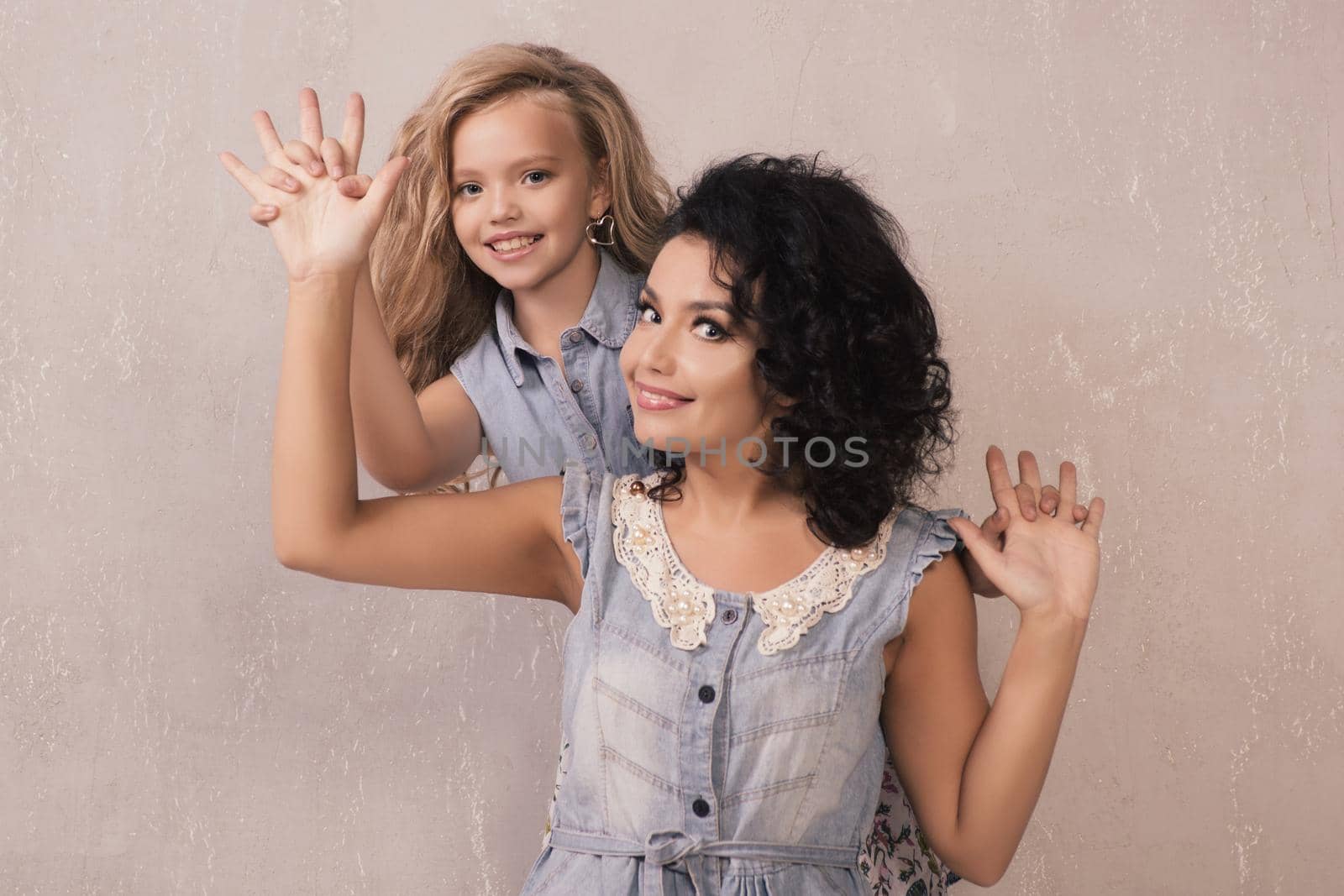 The little girl and the mother dressed in denim dress has fun near a grey wall.