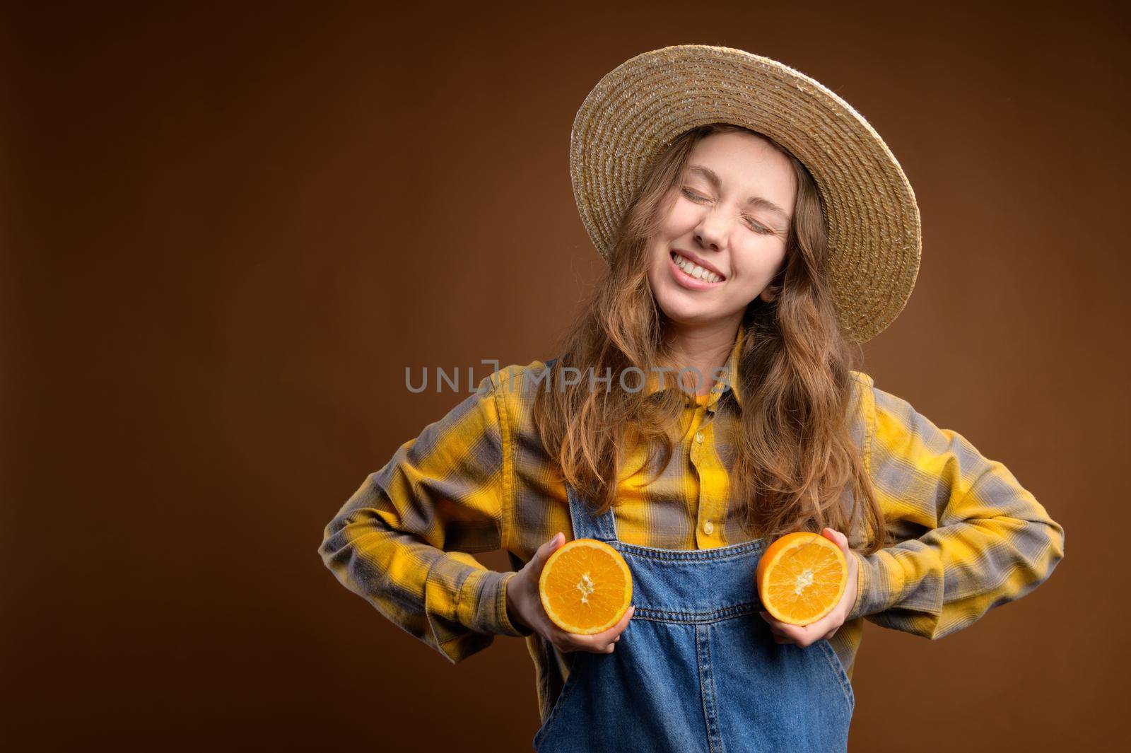 Portrait of adorable pretty playful quirky rural caucasian young woman excited cheerful casual catsuit with happy smile and closed eyes, holding cut oranges on her chest. Metaphor of healthy mammary glands and woman's health.