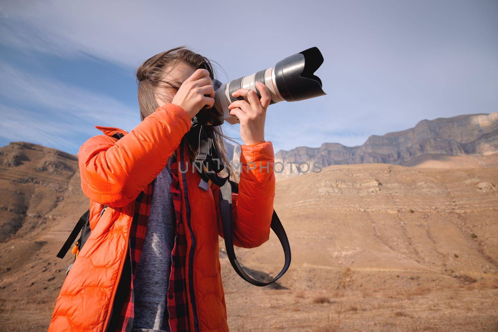 Caucasian woman landscape photographer with big lens and professional camera takes pictures in mountains against background of epic rocks.