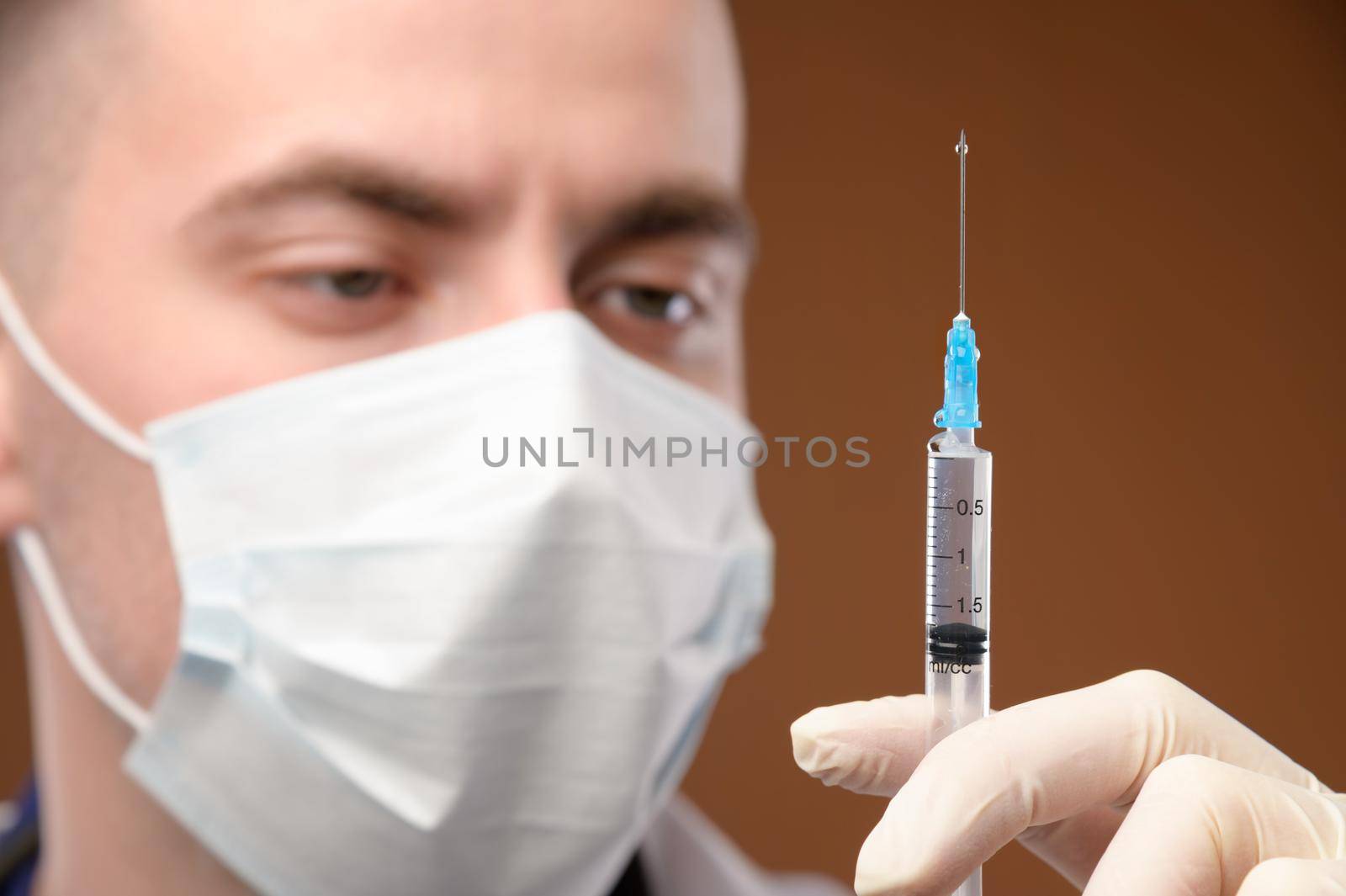 Close-up face of a caucasian doctor preparing a syringe for injection. Young male doctor in a protective mask and gloves holding a syringe with liquid. by yanik88