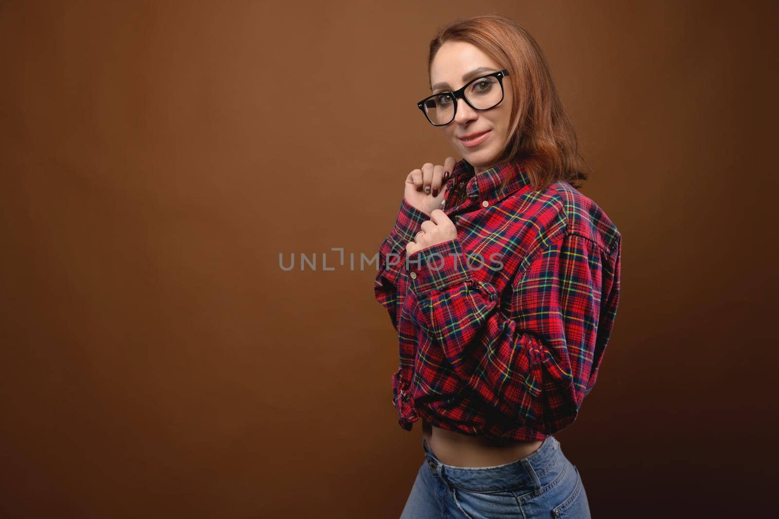 Portrait of a young attractive Caucasian woman in a red shirt and glasses on a brown background. Advertising glasses for improving vision and optics salons by yanik88