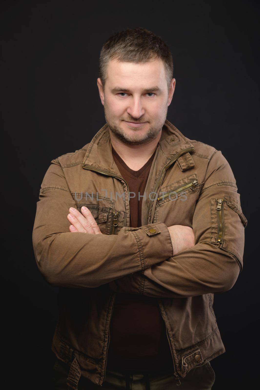Portrait of an attractive Caucasian man in casual clothes. He stands with his arms folded on his chest and looks sternly at the camera with a smile. Studio portrait by yanik88