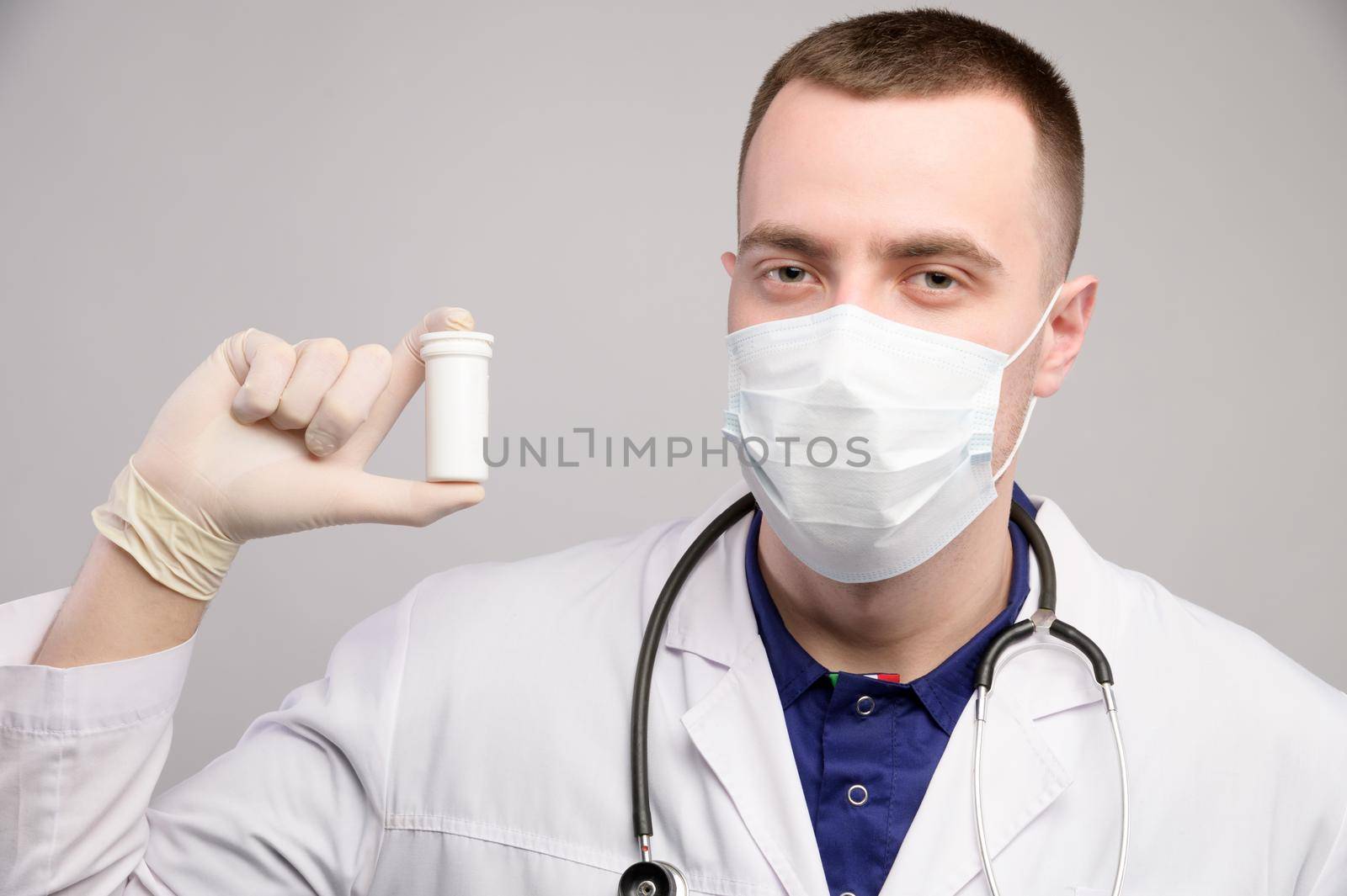 Young caucasian doctor man in a mask and white coat is holding a package with unknown pills. Doctor's recommendation of medications.