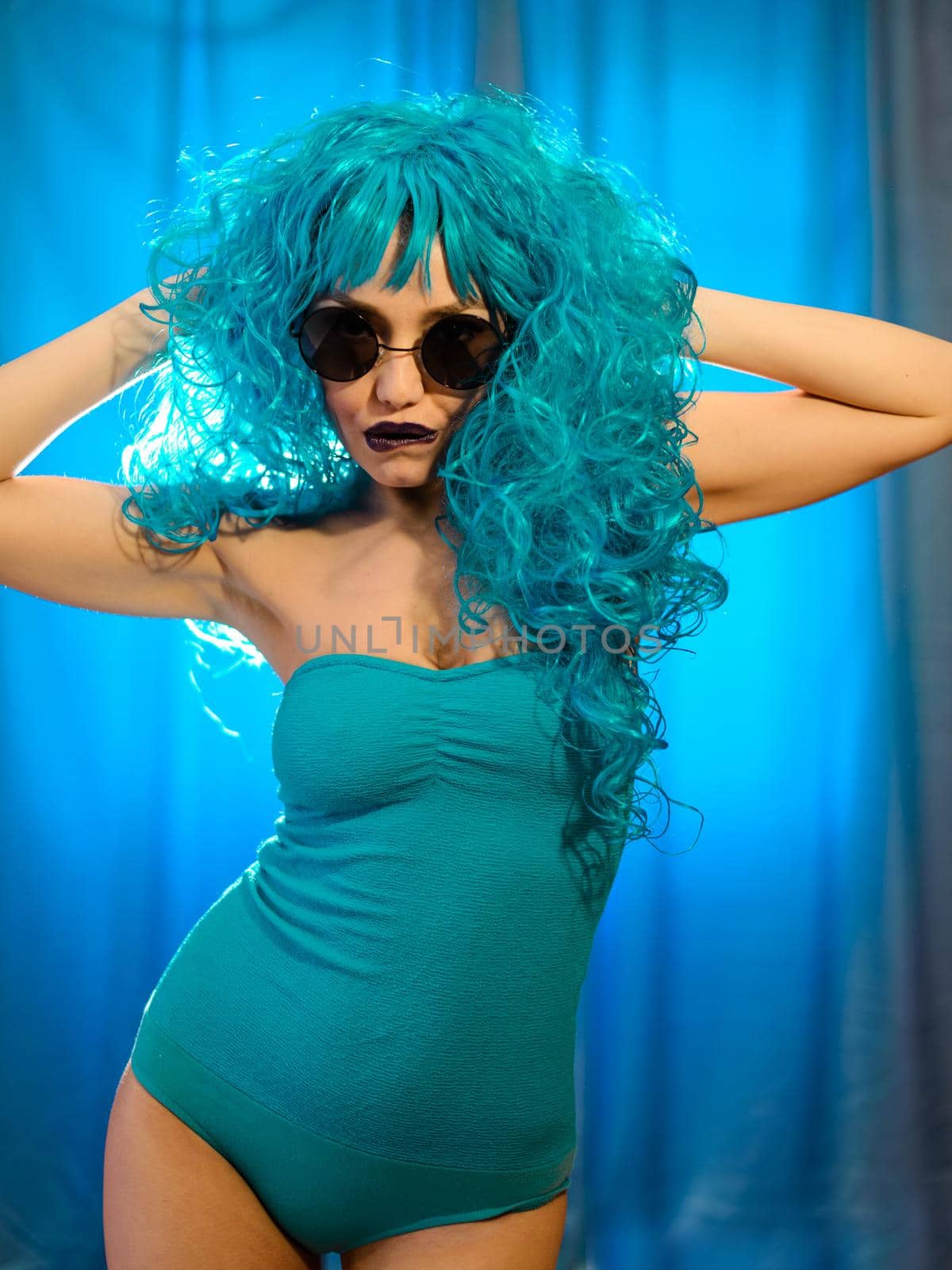 Girl in a blue body suit with blue hair and sunglasses