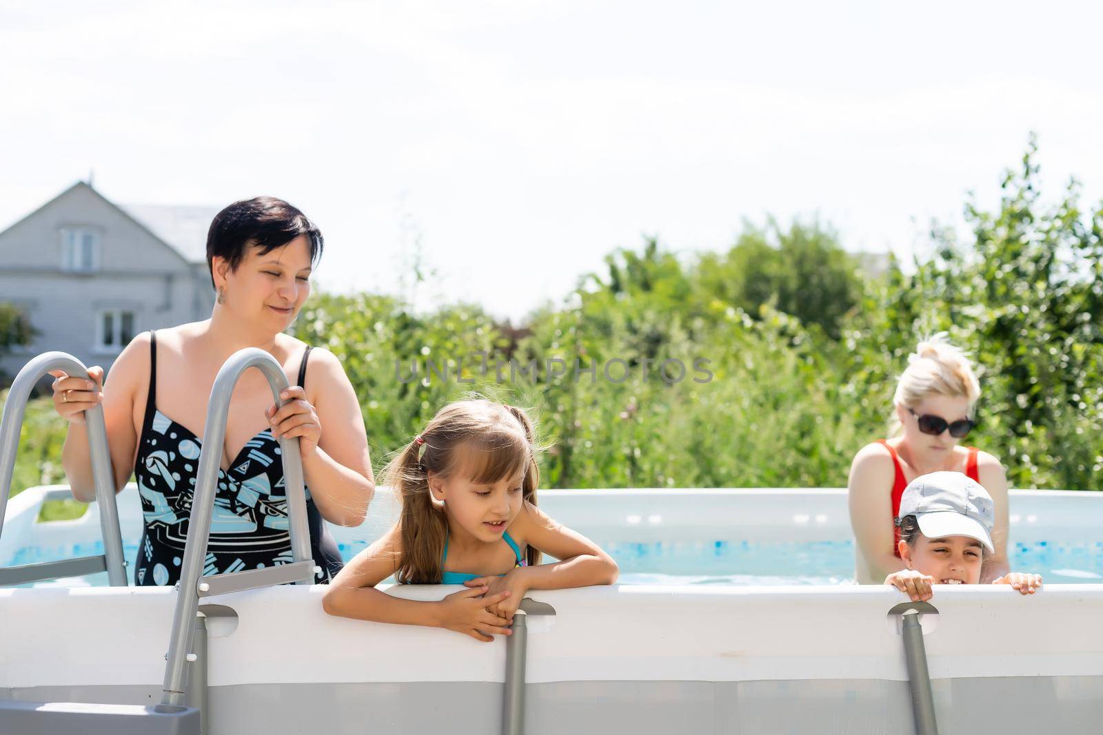 Mother and two daughters playing in pool water.Woman and two girls have fun in home pool splashing water and smiling by Andelov13