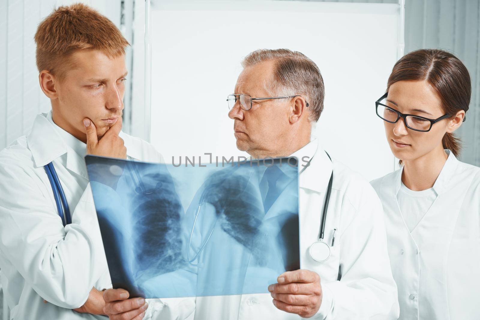 Professor older man doctor and young doctors examine x-ray image of lungs in a hospital