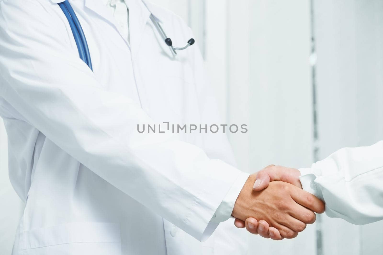 Man doctor shakes hand with another doctor in hospital, close-up image, face is not visible, concept of teamwork