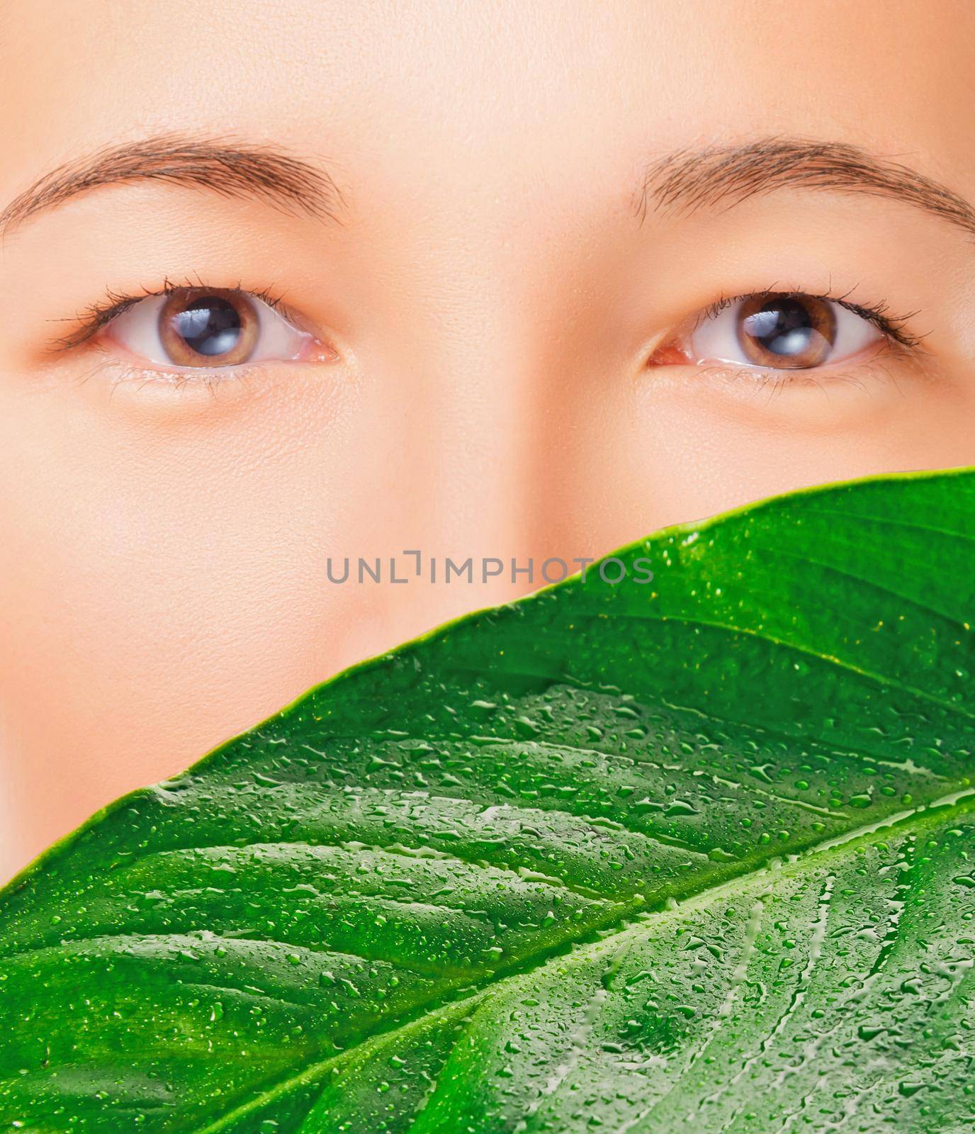 Face of beautiful woman is covered by green leaf, concept of beauty and eco