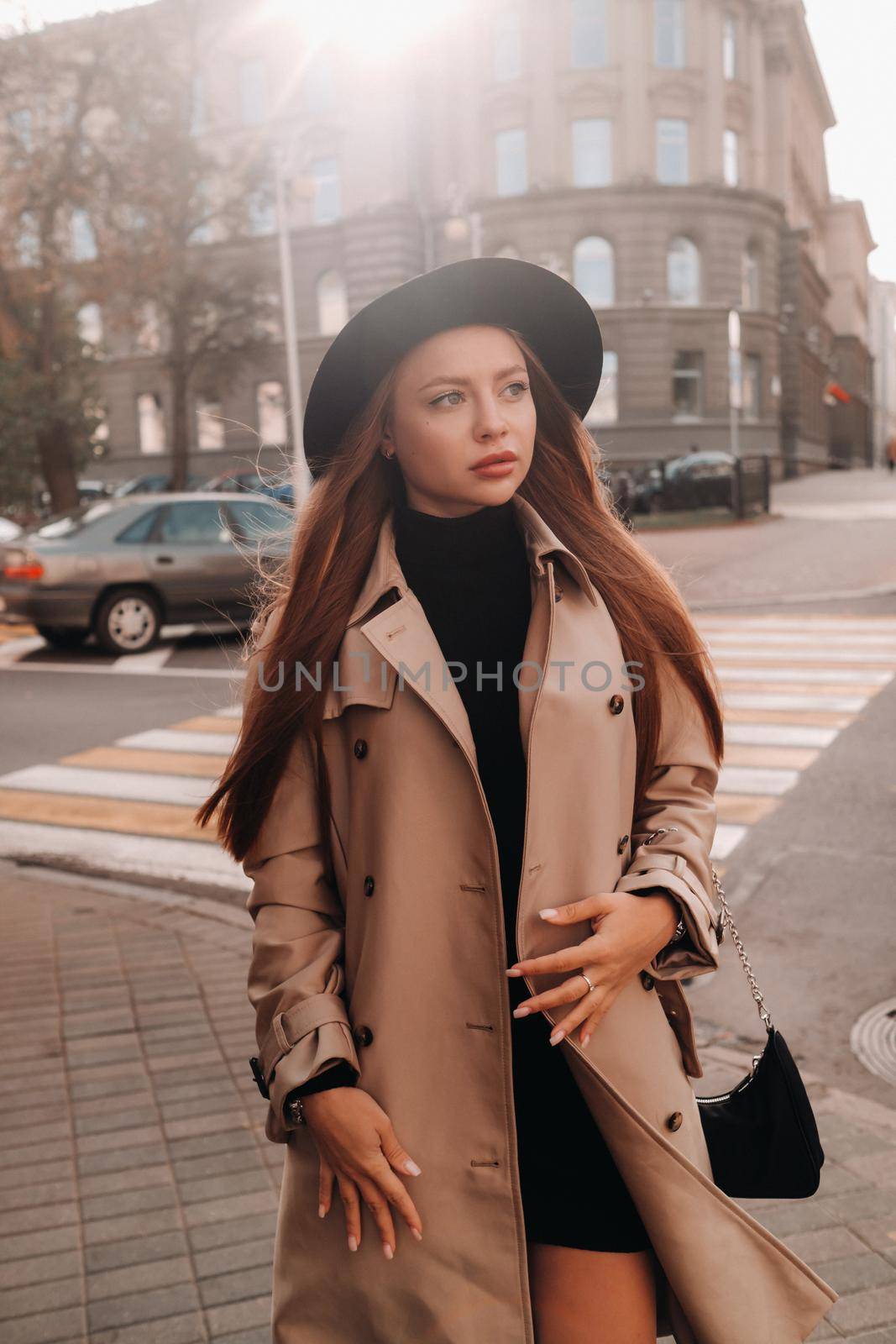 Stylish young woman in a beige coat in a black hat on a city street. Women's street fashion. Autumn clothing.Urban style.