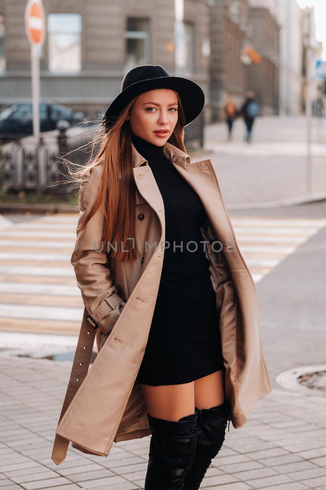 Stylish young woman in a beige coat in a black hat on a city street. Women's street fashion. Autumn clothing.Urban style.