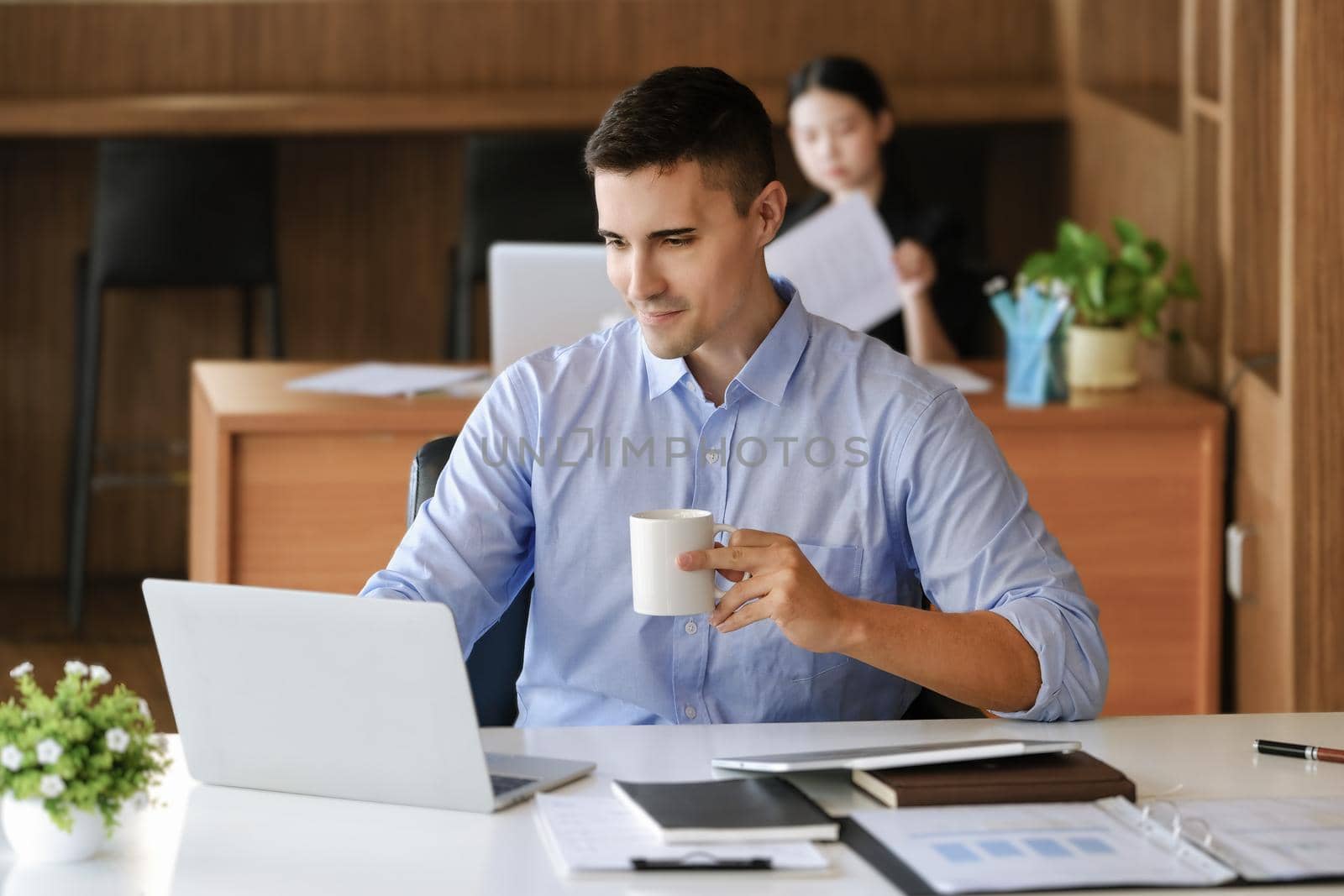 Male marketing managers drink coffee while working to reduce drowsiness before using computers, iPads, and marketing analysis papers. by Manastrong