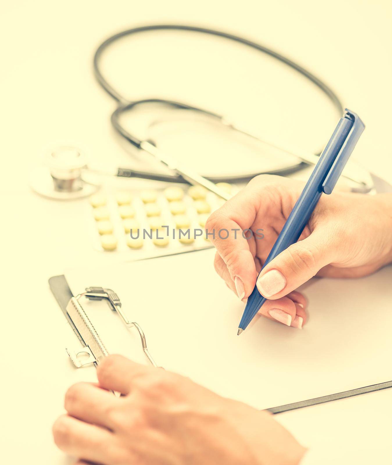 doctor writing a prescription at the workplace with pills and stethoscope