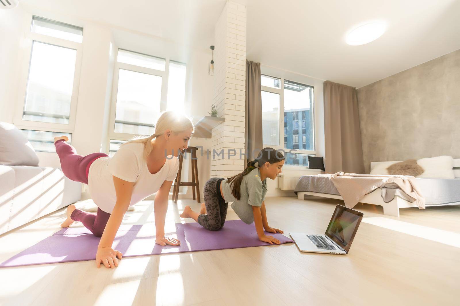 Young adult mother with her daughter watching online training together at home, looking a laptop