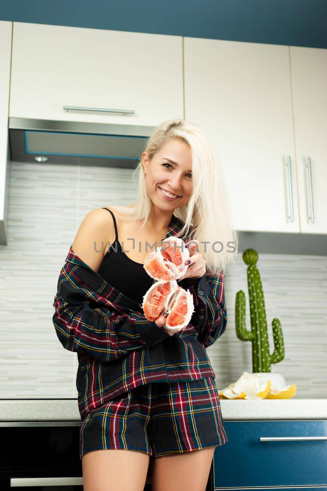 the woman in the kitchen in home clothes with a peeled pomelo fruit smiles