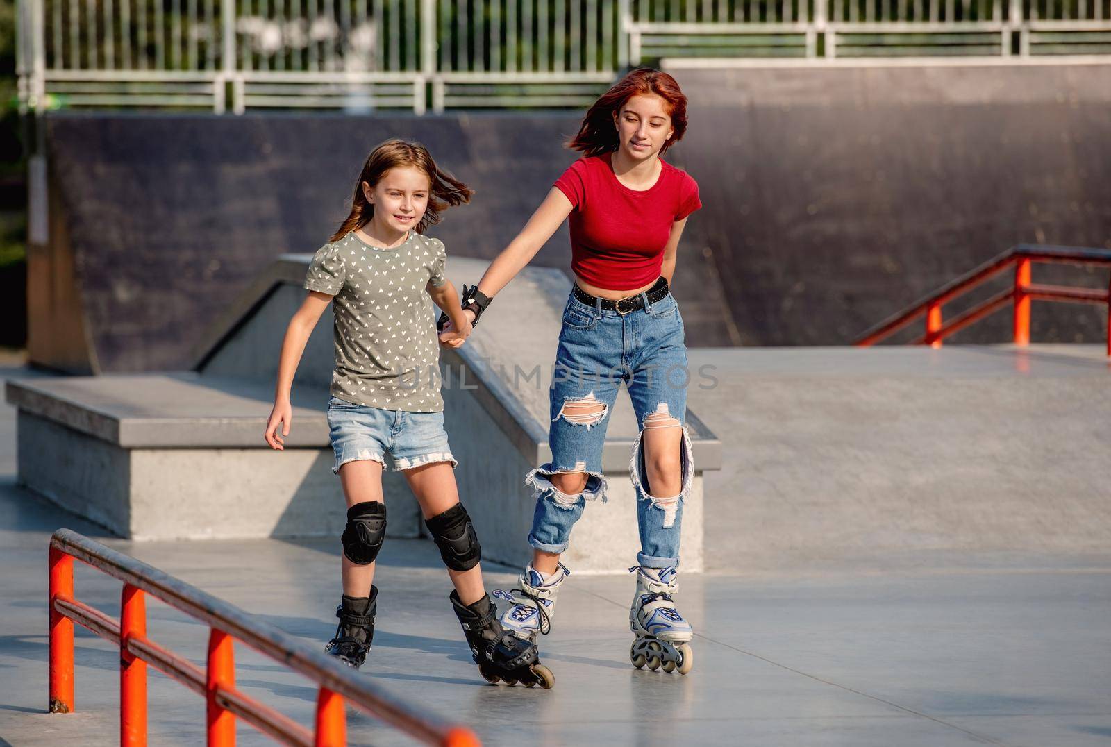 Two girls wearing roller skates riding together at park ramp. Sisters rolleblading outdoors at summer
