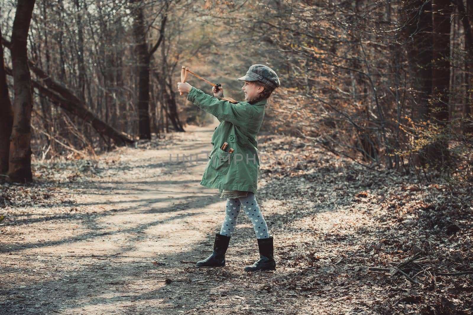little girl playing with a slingshot in the woods, photo in vintage style