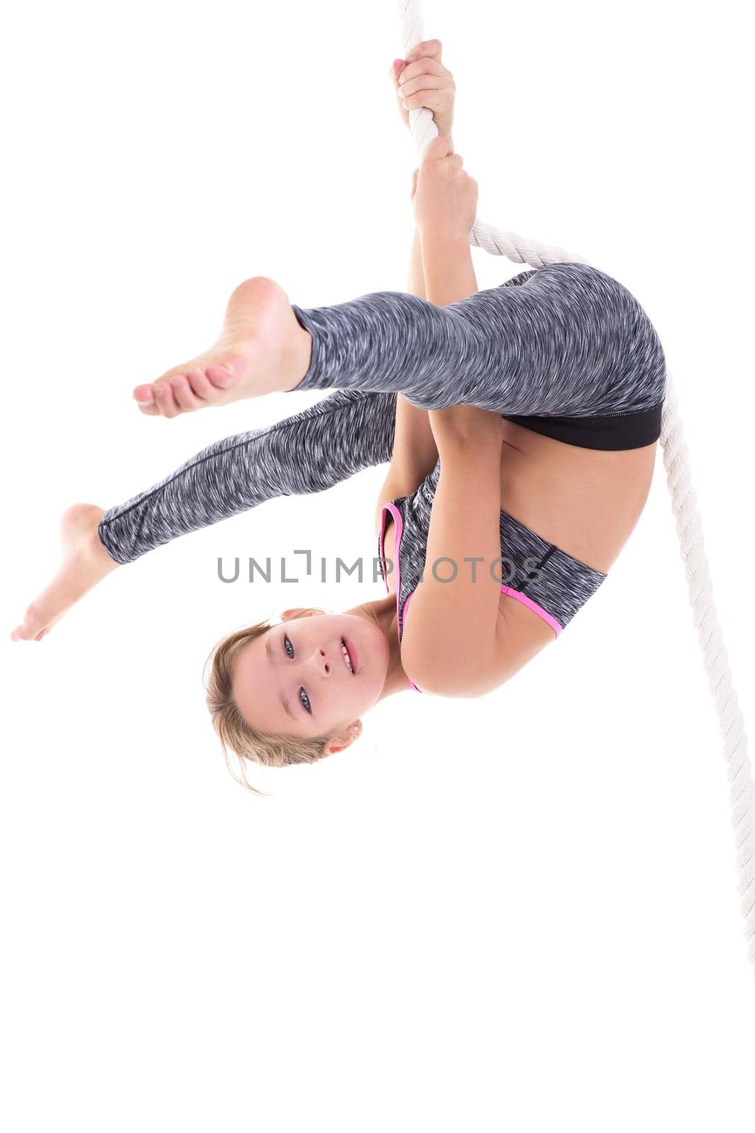 Girl flipping upside down on rope. Smiling child wearing sports clothes exercising on rope against white background. Happy childhood, active lifestyle concept