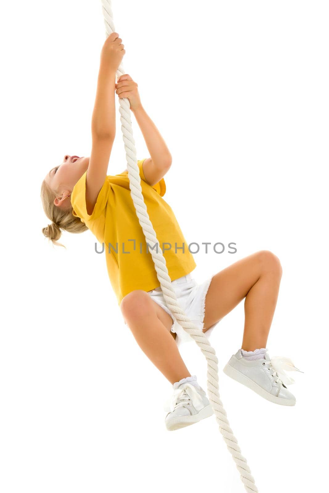 Cheerful little girl holding a rope with her hands. She tries to swing from side to side on it. Sport, fitness concept. Isolated over white background.