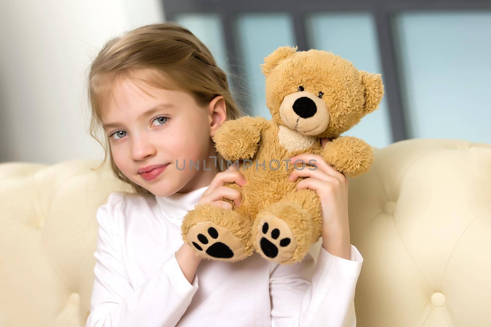 Little girl on sofa hugging teddy bear. by kolesnikov_studio