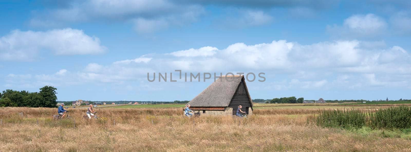 people on bicycle near typical barn on the island of texel in the netherlands by ahavelaar