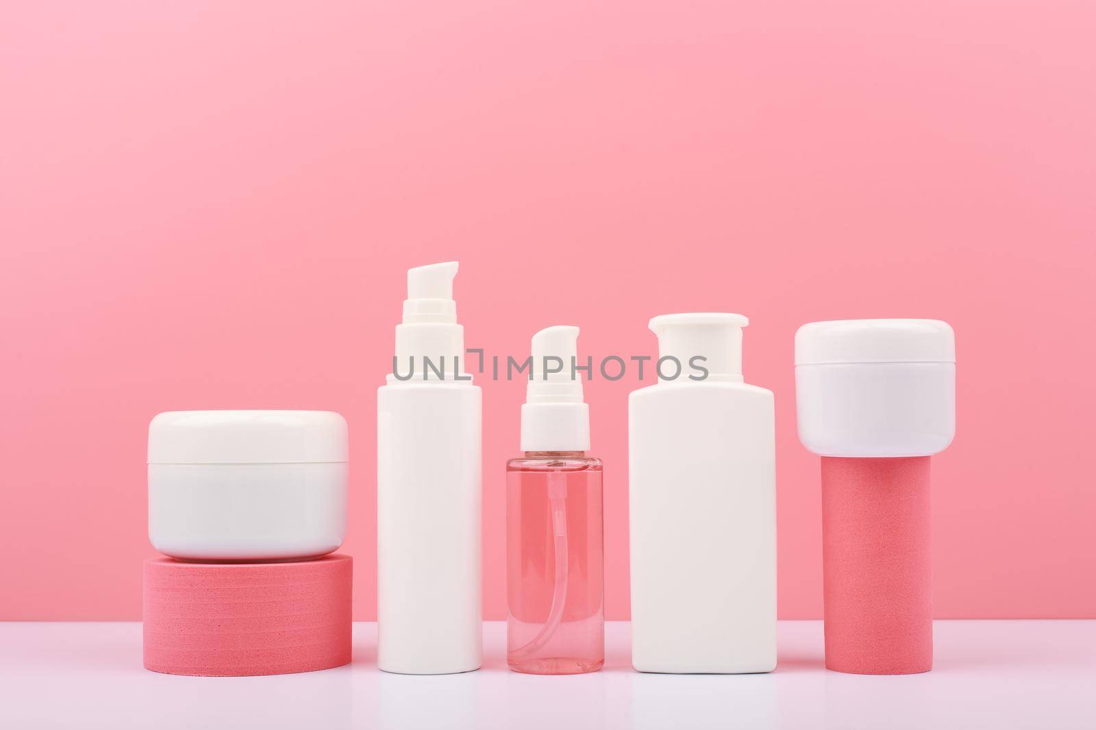 Trendy composition in pink colors with set of cosmetic bottles with beauty products on geometric props against pink background. Concept of organic cosmetics for anti acne or anti aging treatment