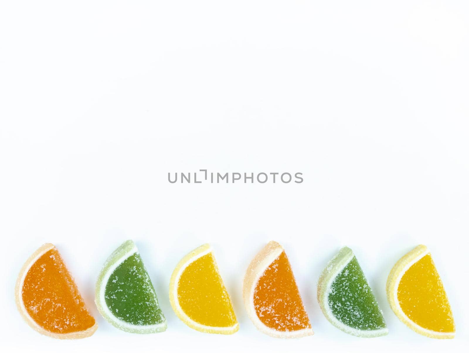Multicolored marmalade citrus slices in sugar on a white background with copy space.