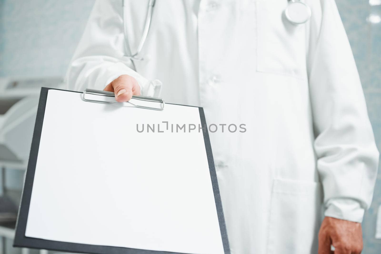 Unrecognizable older doctor holds out empty clipboard, space for text