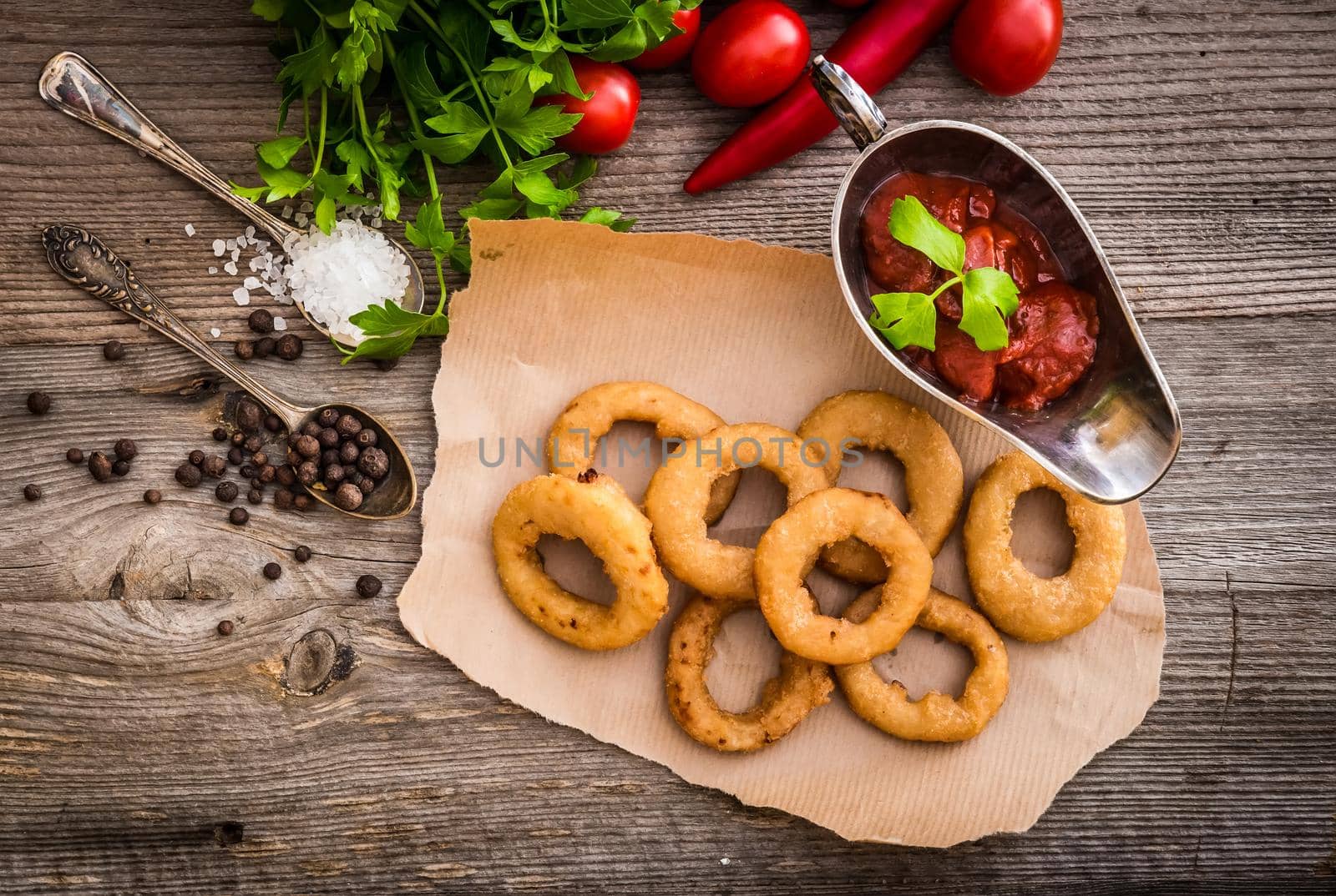 fried onion rings on parchment with sauce and vegetables on a wooden background