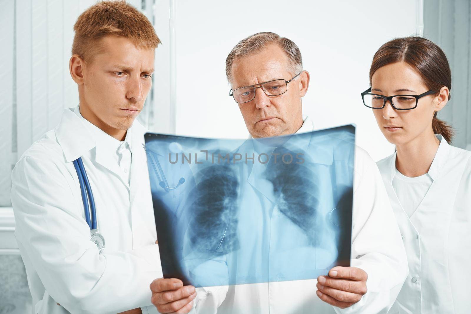 Older man doctor and young doctors examine x-ray image of lungs in a clinic