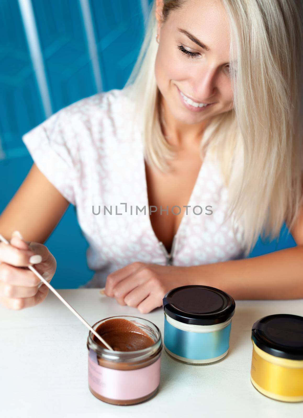 Blonde woman sits at a table with vegan paste in jars by Rotozey