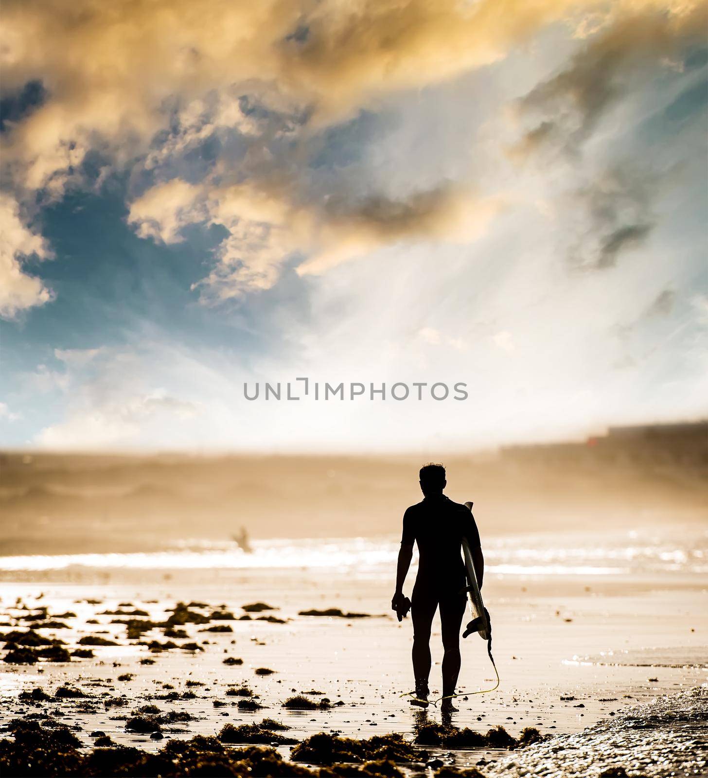 Silhouette of man with a surfboard on the beach at sunset