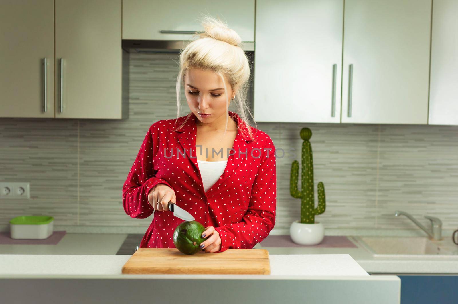 the blonde vegan woman cuts avocado in kitchen