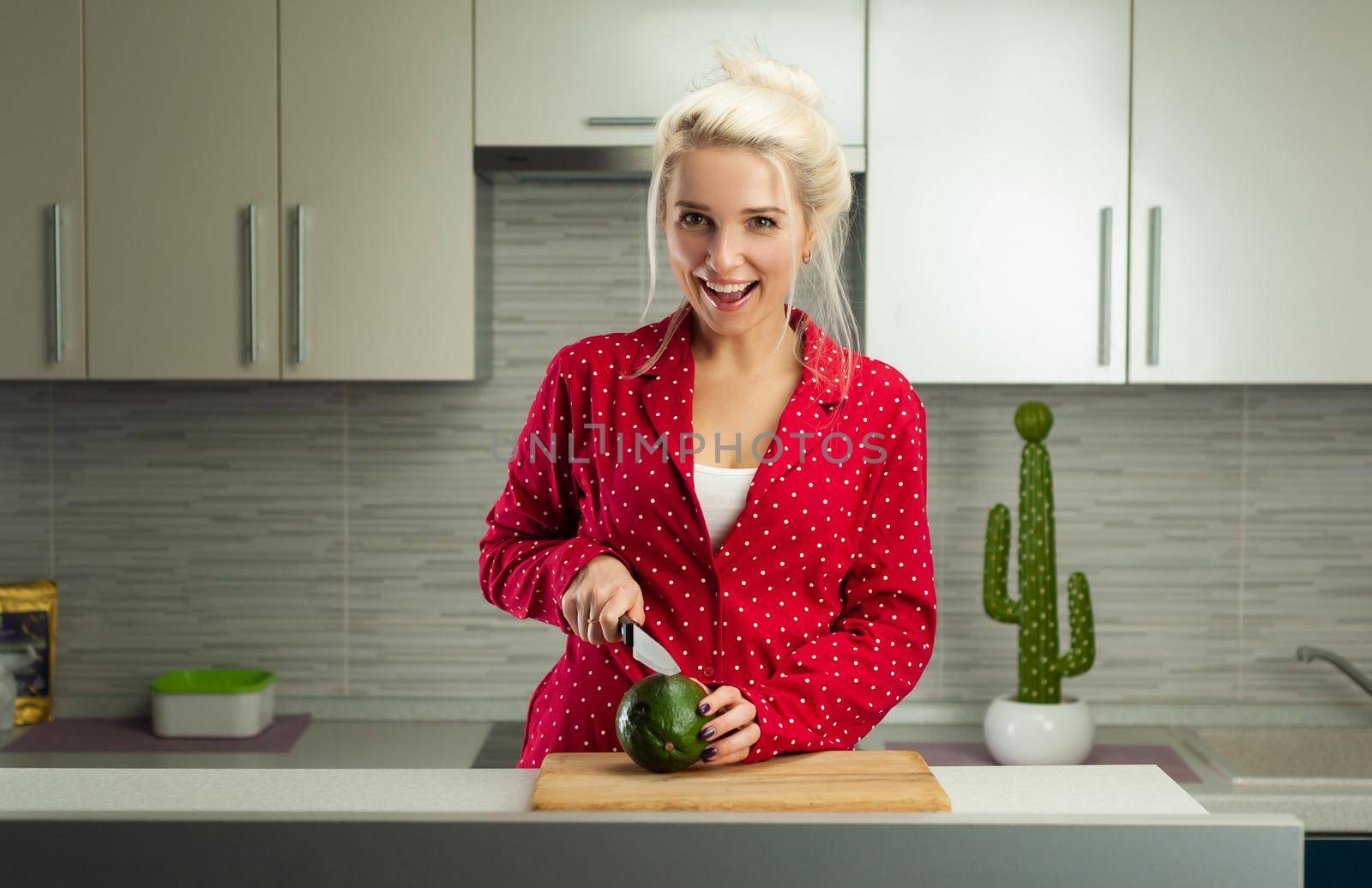 blonde vegan woman cuts avocado in kitchen by Rotozey