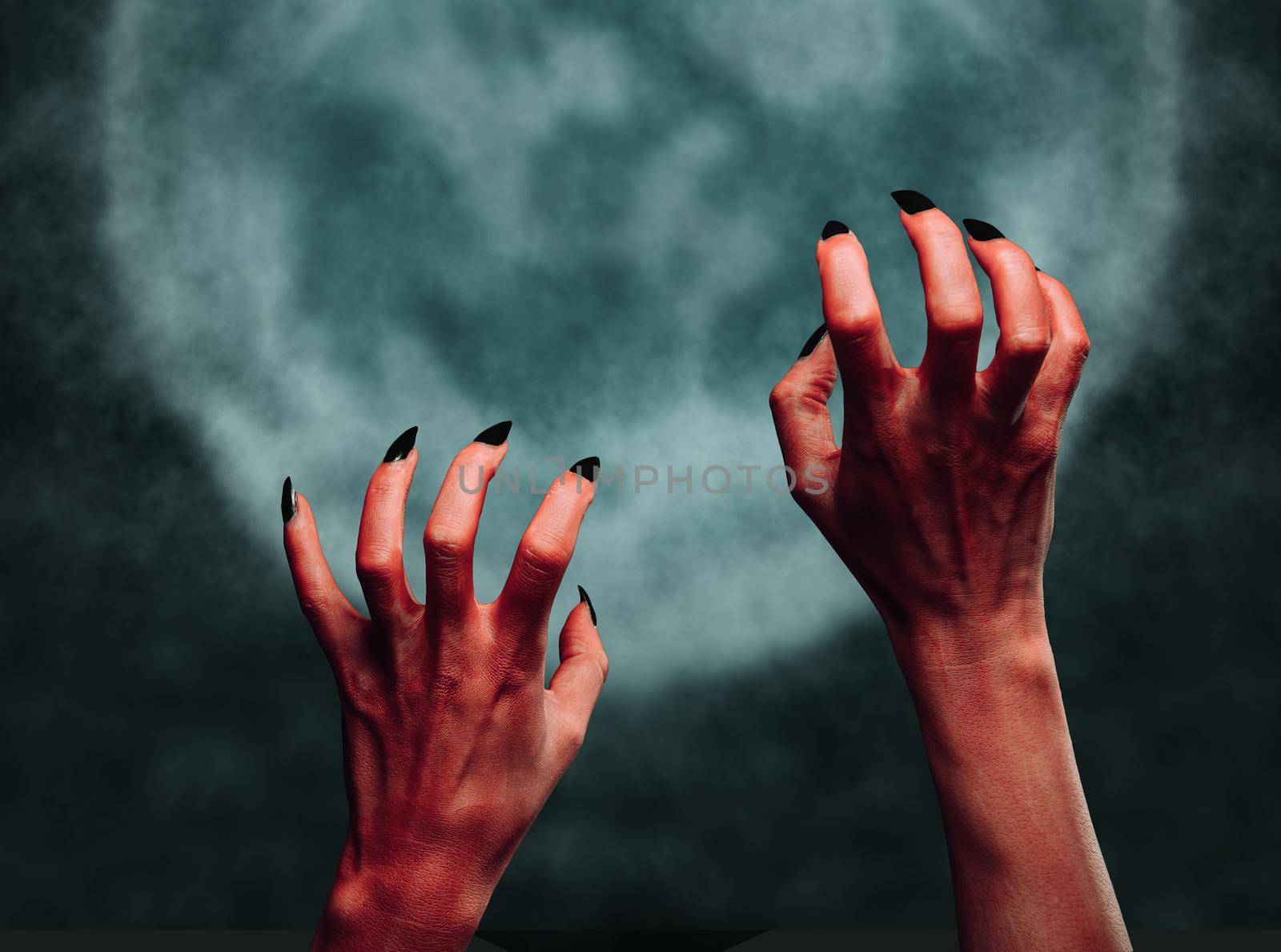 Red hands of the demon on background of full moon. Halloween or horror theme