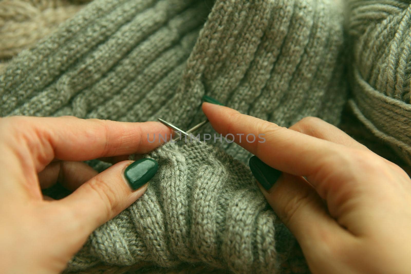 Knitting - young womans hands using knitting needles and grey wool roll. woman hands knitting scarf